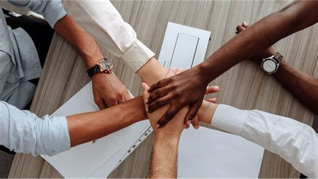 A group of people coming together with their hands clasped in a show of teamwork.