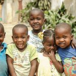 Several youngsters, wearing bright smiles, stand together and pose happily for a photograph.