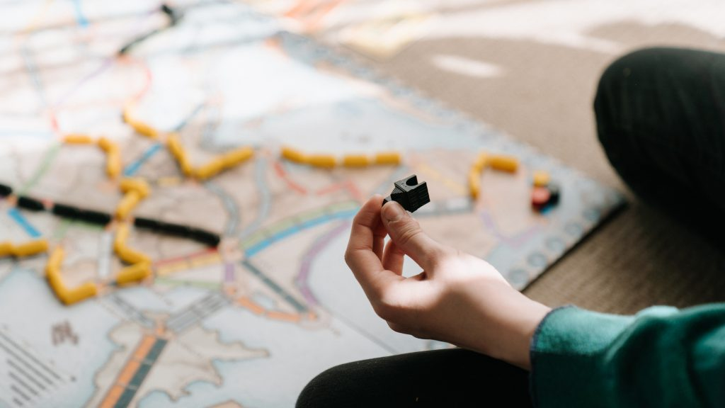 A person engaged in a board game involving a train, strategically maneuvering game pieces on a colorful game board.