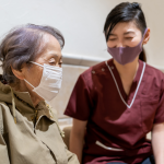 A nurse and an elderly woman, both wearing face masks, demonstrate responsible health practices during the pandemic.