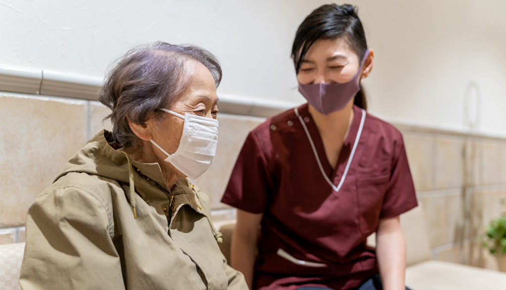 A nurse and an elderly woman, both wearing face masks, demonstrate responsible health practices during the pandemic.