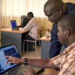 Two individuals collaborating on a laptop computer amidst an educational setting.