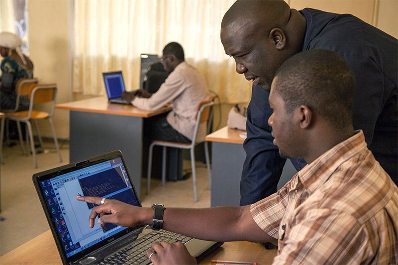 Two individuals collaborating on a laptop computer amidst an educational setting.