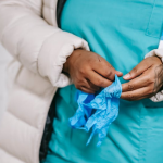 A female nurse wearing a hospital gown is holding a blue bandana in her hand.