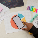 n individual focused on their smartphone, surrounded by a cluttered table adorned with papers and pens.